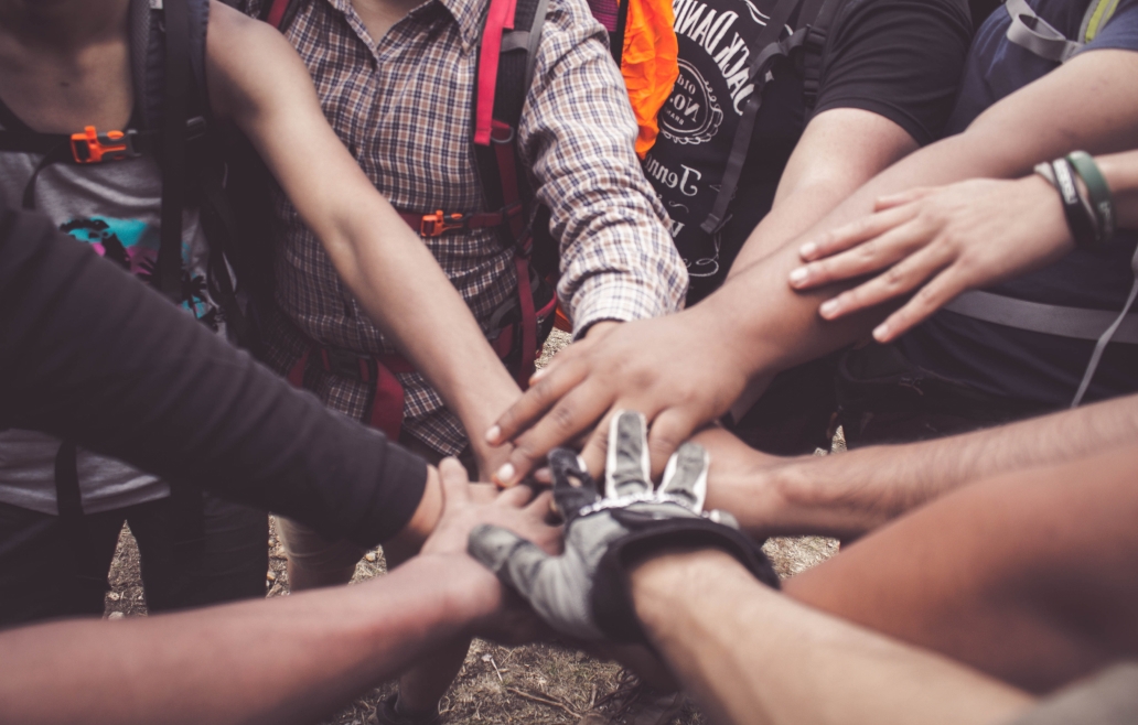 A team of outdoorsmen and women put their hands together for a cheer.